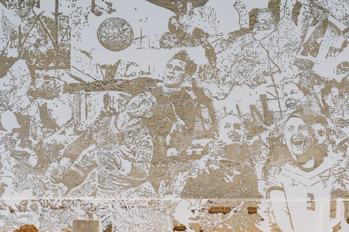 Painel artístico de grande escala criado por Vhils na fachada do Estádio da Tapadinha, composto por retratos, cenas associadas ao Atlético Clube de Portugal e elementos gráficos gravados na superfície do edifício através da remoção de camadas do revestimento.