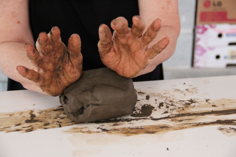 Hands shaping clay on a workbench