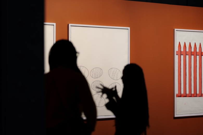 Silhouette of two people with paintings in the background, against an orange wall