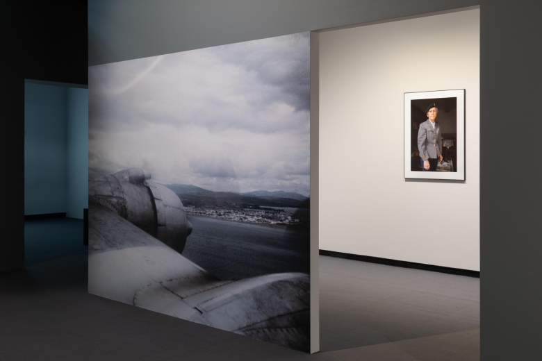 Panel showing an aerial view over a beach, with a portrait of a woman soldier in the background of the gallery. 