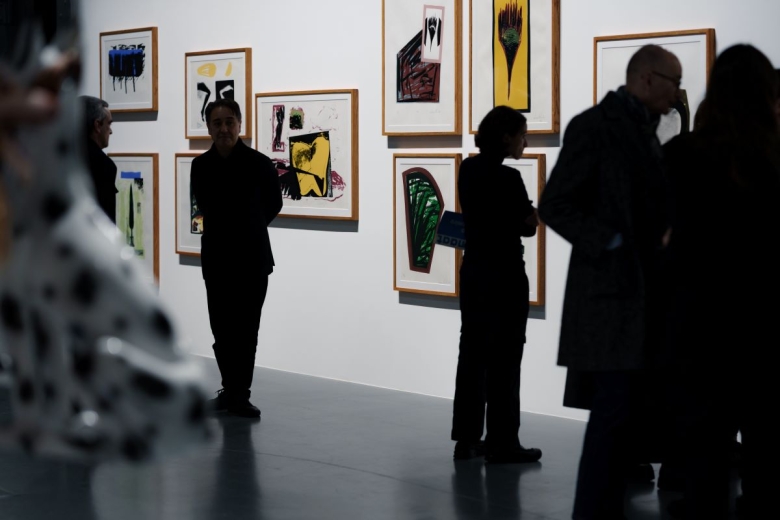 Silhuetas de pessoas numa sala do MAAT, com gravuras do artista Sérgio Pombo penduradas numa parede branca