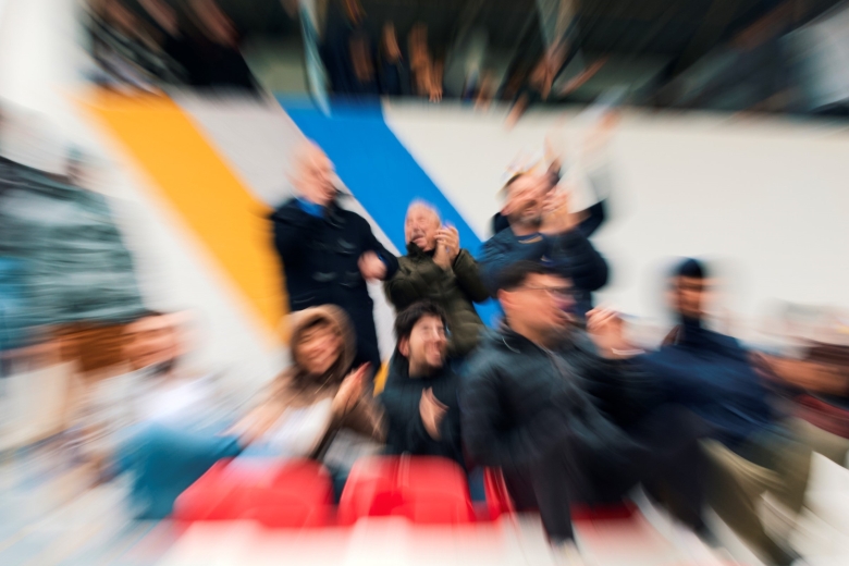 Group of people seated in a stadium stand, photographed with a blur and motion effect.