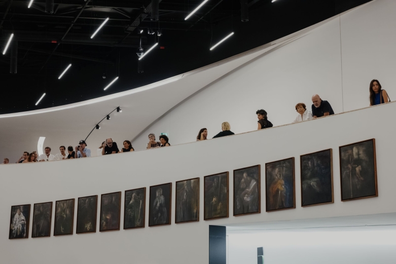 Visitantes observam a exposição de Pedro Cabrita Reis no MAAT Central, junto a uma varanda curva com vista para uma série de pinturas.