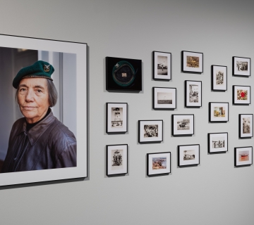 Large photograph of a woman soldier, sided by smaller black-and-white photographs, hung on a white wall.